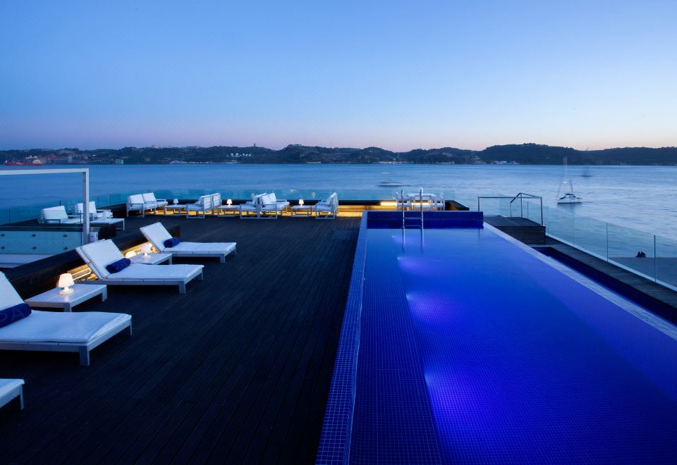 a luxurious yacht with multiple swimming pools and sun loungers on its deck , overlooking the water and mountains at Altis Belem Hotel & Spa, a Member of Design Hotels