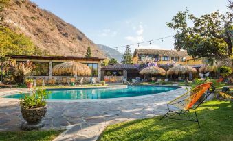 a beautiful swimming pool surrounded by lush greenery and mountains , with straw huts in the background at Selina Atitlan