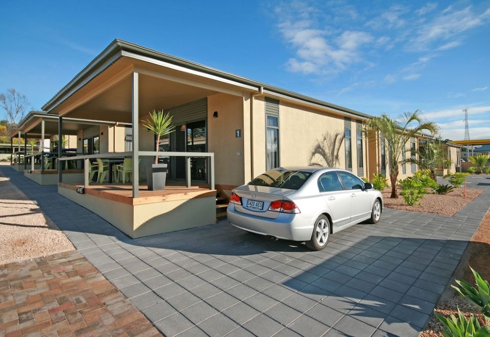 a silver car is parked in front of a beige house with a porch and palm trees at Streaky Bay Hotel Motel