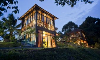 a wooden house with a balcony is lit up at night , surrounded by trees and bushes at Bilut Hills @ Bentong