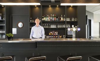 a man is standing behind a bar in a hotel , preparing to serve drinks to customers at Ibis Luxembourg Sud