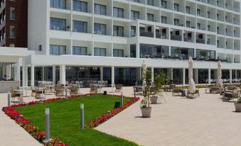 a large white building with many windows is surrounded by a paved area with flowers and chairs at The Ivi Mare - Designed for Adults by Louis Hotels