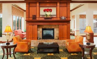 a living room with a fireplace , two orange chairs , and a table in front of it at Hilton Garden Inn Omaha West