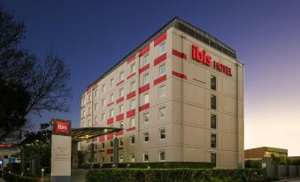 "a large hotel building with the name "" ibis "" displayed on its side , surrounded by trees" at Ibis Sydney Airport