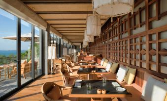 a restaurant with wooden tables and chairs , large windows , and hanging lights , giving it an inviting atmosphere at Six Senses Krabey Island