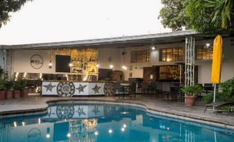 a large swimming pool with a bar and lounge area in front of it , surrounded by trees at Fawlty Towers Guest House