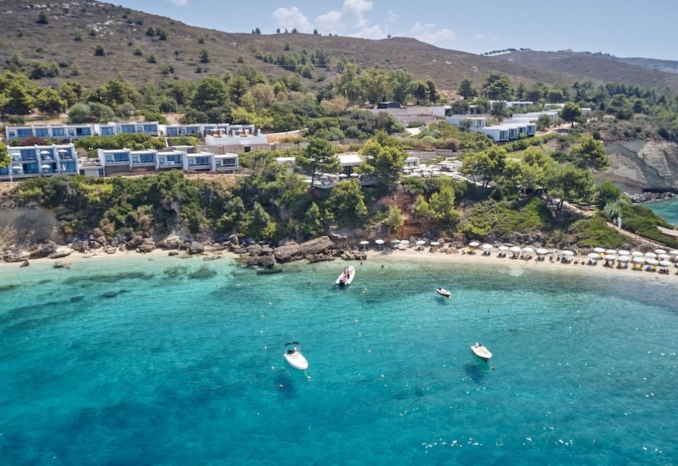 a picturesque beach scene with several boats floating in the water , surrounded by lush green hills at White Rocks Hotel Kefalonia