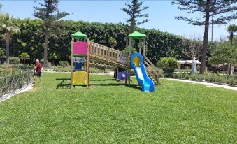 a colorful playground with a slide and other play equipment in a grassy area at Hotel Flora