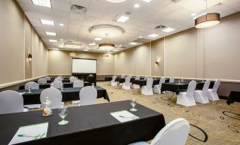 a large conference room with rows of tables and chairs , a projector screen , and two wine glasses on each table at Holiday Inn Morgantown - Reading Area
