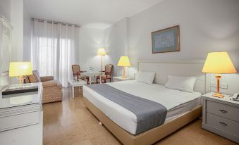 a large bed with a gray blanket is in the middle of a room with two chairs and lamps at Grand Hotel Madaba