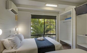 a bedroom with a bed , white walls , and a sliding glass door leading to a balcony at Discovery Parks - Ballina