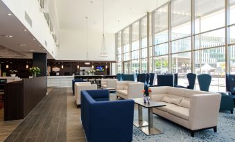 a modern lounge area with blue and white couches , chairs , and tables in a spacious room at Hampton by Hilton Oswiecim