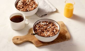 a wooden cutting board with two bowls of granola and a cup of coffee , accompanied by orange juice and coffee at TownePlace Suites Clovis