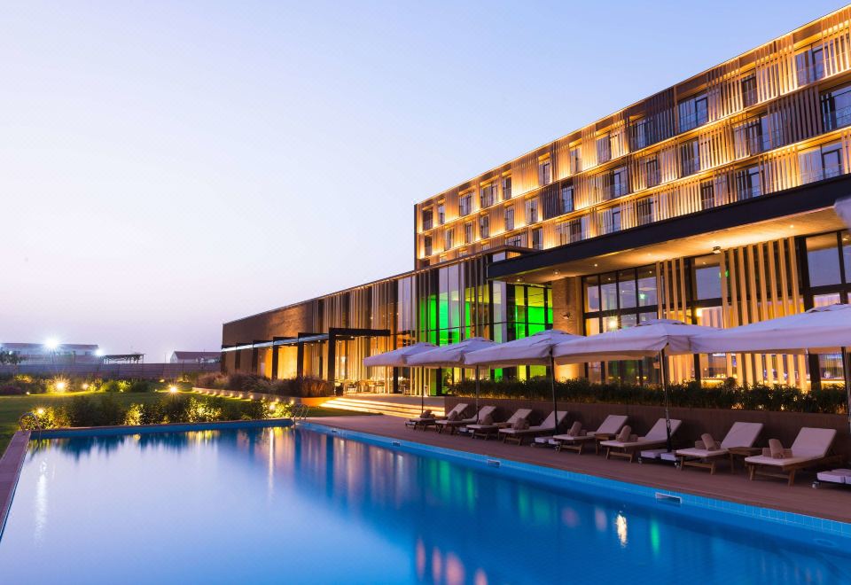 a large hotel with a swimming pool and surrounding lounge chairs , all lit up at night at Radisson Hotel, Dakar Diamniadio