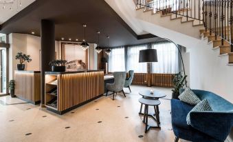 a modern hotel lobby with a large reception desk , blue chairs , and a staircase leading to the second floor at Hotel Post Alpine Cityflair