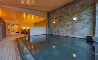 a large indoor swimming pool with a stone wall and wooden ceiling , surrounded by modern lighting at Fuji Matsuzono Hotel