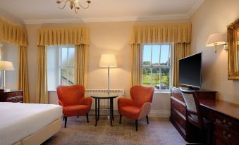 a cozy bedroom with two red chairs , a television , and a window overlooking a golf course at Delta Hotels Breadsall Priory Country Club