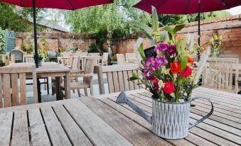a wooden table with a vase of flowers and an umbrella in the background of an outdoor dining area at The Boot Inn