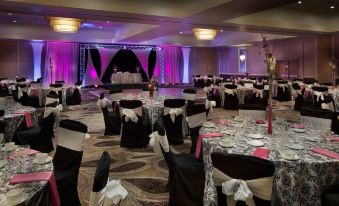 a large banquet hall with black and white tables and chairs , purple lighting , and pink curtains at Hilton Concord