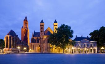 a large church with a tall steeple is illuminated at night , surrounded by a large open square at Novotel Maastricht