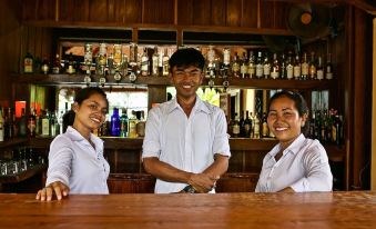 three people standing behind a bar , smiling at the camera while surrounded by various bottles and glasses at Rikitikitavi