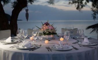 a beautifully set dining table with white linens , wine glasses , and a centerpiece of flowers at Aphrodite Beach Hotel