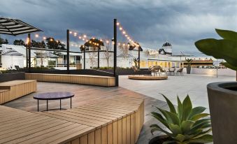 a modern outdoor area with wooden benches , umbrellas , and lights , surrounded by a cloudy sky at Tradewinds Hotel and Suites Fremantle