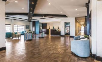 a modern , well - lit lobby with wooden flooring and blue chairs arranged around a central table at La Quinta Inn & Suites by Wyndham Dallas Grand Prairie South
