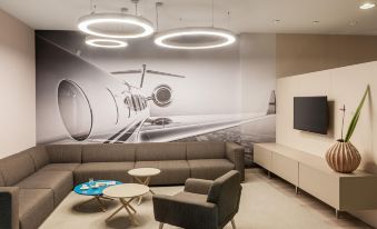 a modern office space with a large airplane mural on the wall , a couch , chairs , and a coffee table at NH Vienna Airport Conference C