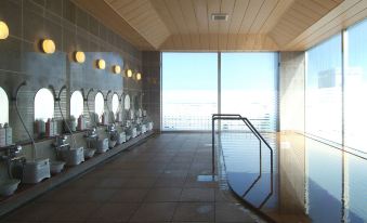 a modern swimming pool area with multiple sinks and mirrors , overlooking the ocean , under a wooden ceiling at Route Inn Grantia Hakodate Ekimae