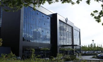 a large building with a black facade and glass windows is surrounded by green grass at Village Hotel Farnborough