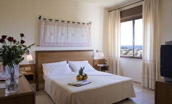 a large bed with white linens and a wooden headboard is in a room with two lamps , a window , and a colorful tapestry on at Hotel Califfo