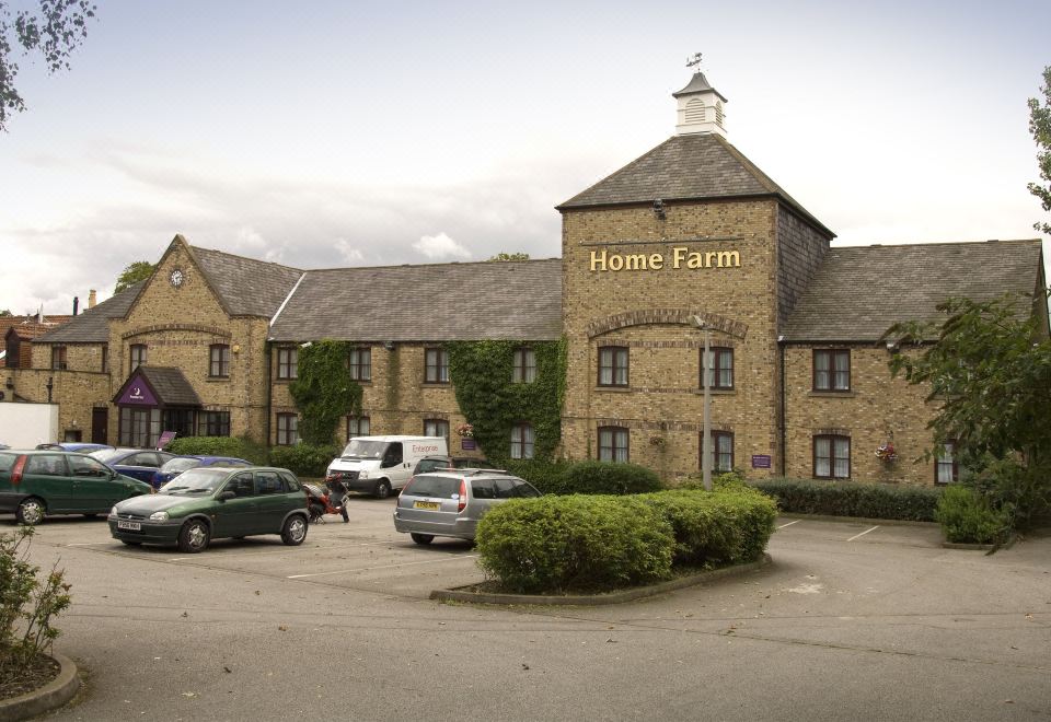 "a large building with a sign that says "" home farm "" is surrounded by parked cars and bushes" at Premier Inn Hull West