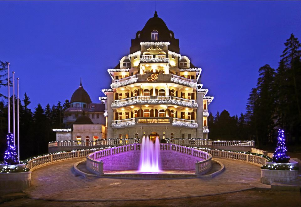 a large , ornate building with a fountain in front of it , illuminated at night at Festa Winter Palace Hotel