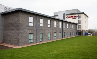 "a modern , gray - brick building with the sign "" hampton inn "" on top , surrounded by green grass and trees" at Hampton by Hilton Exeter Airport