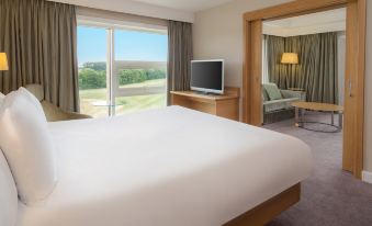 a large bed with white sheets is in a room with a window and a television at Hilton at St.George's Park, Burton Upon Trent