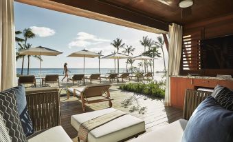 a beach house with a large deck overlooking the ocean , where several chairs and umbrellas are set up for relaxation at Four Seasons Resort Oahu at Ko Olina