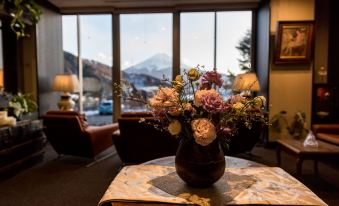 a vase with flowers on a table in front of a window , overlooking a mountain at Mizno Hotel