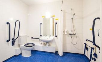 a small bathroom with blue flooring , white walls , and various accessories such as a toilet , sink , shower , and grab bars at Travelodge Ludlow Woofferton
