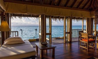 a cozy living room with a couch and chairs , overlooking the ocean through a window at Gili Lankanfushi Maldives