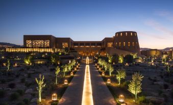 a long , narrow walkway lined with trees and lit up in front of a large building at dusk at Anantara Al Jabal Al Akhdar Resort
