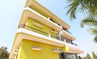a modern , yellow and white building with multiple balconies , situated next to palm trees under a clear blue sky at Collection O 27949 Hotel Kriti Green