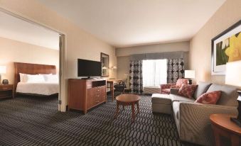 a hotel room with a couch , coffee table , television , and bedroom door open to a bedroom at Hilton Garden Inn Akron-Canton Airport