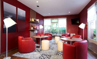 a modern lounge area with red walls , wooden floors , and various seating options such as chairs and tables at Campanile Rouen Est - Franqueville Saint Pierre