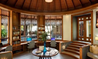 a wooden lounge area with a round table and chairs , surrounded by windows and bookshelves at Anantara Dhigu Maldives