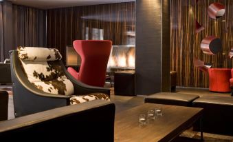 a modern living room with a red chair and cowhide ottoman , wood paneling , and a coffee table at Avenue Lodge Hotel & Spa