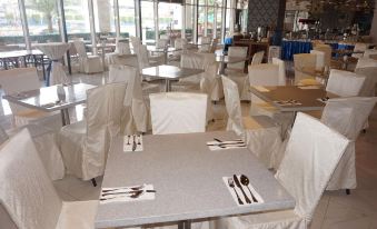 a restaurant with white tables and chairs , covered in white tablecloths and napkins , has several other tables with cutlery in the background at Hotel 101 Manila
