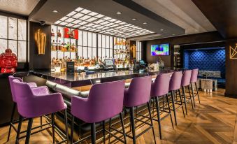 a modern bar area with a long wooden bar , several stools , and a television mounted on the wall at The Kingsley Bloomfield Hills - a DoubleTree by Hilton