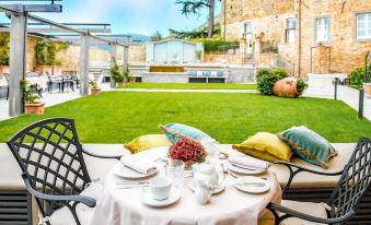 a table set with tea and flowers in front of a stone building , surrounded by greenery at Monastero di Cortona Hotel & Spa