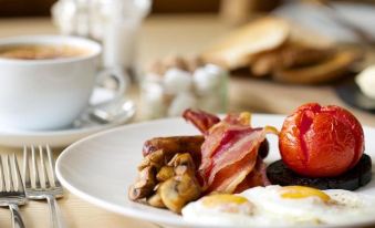 a plate of food on a dining table , consisting of eggs , bacon , mushrooms , and a cup of coffee at The Star